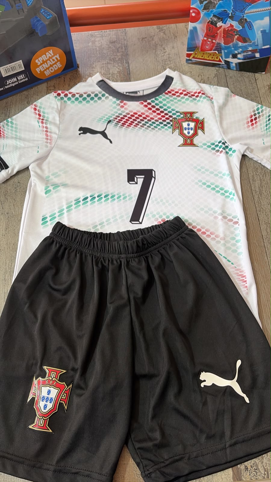 Portugal Puma home kids football kit number 7 Ronaldo white jersey with red green dot pattern and black shorts flat lay