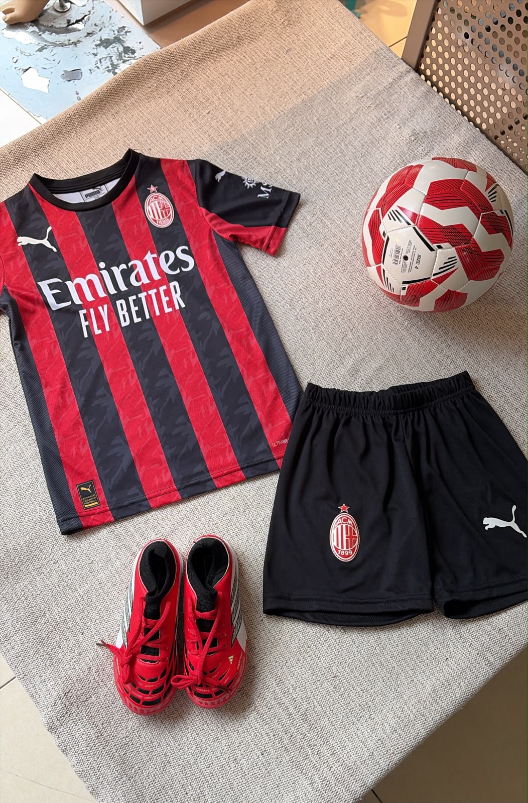 AC Milan kids football kit red and black stripes jersey Emirates sponsor and black shorts flat lay
