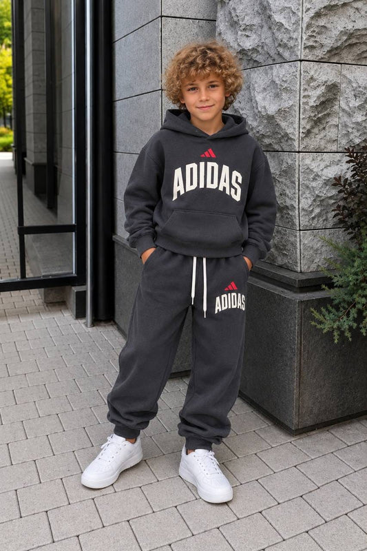 Child wearing charcoal Adidas hoodie and matching joggers with red logo accents