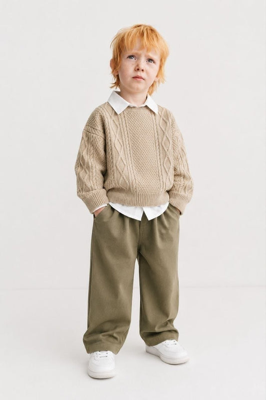 Boy wearing beige cable-knit sweater, white collared shirt and olive trousers
